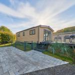 Holzhaus mit Terrasse, Grill und gepflastertem Hof im Wald.