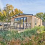 Holzhaus mit Terrasse, Grill und Garten. Umgeben von Bäumen und Grünflächen.