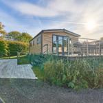 Holzhaus mit Terrasse, Grill und Garten. Zugang über gepflasterten Weg.