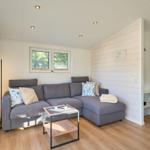 Ein Wohnzimmer mit grauem Sofa, Tisch und Fenster. Holzfußboden und Holzwand.