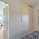 Schlafzimmer mit Bett, Kleiderschrank und Fenster. Durchgang zur Küche und Wohnfläche.