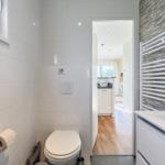 Badezimmer mit Toilette, Waschtisch und Heizung. Blick in die Küche.