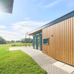Moderne Holzhäuser mit Terrasse und Garten. Blick auf Felder und Bäume.