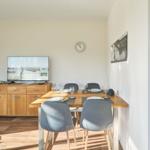 Essbereich mit Tisch, Stühlen und Fernseher. Wanduhr und Bild an der Wand.