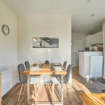 Essbereich mit Tisch, Stühlen und Wandbild. Küche und Wohnbereich im Hintergrund.