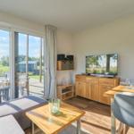 Wohn- und Essbereich mit TV, Tisch und Sofa. Durchgang zur Terrasse mit Gartenblick.