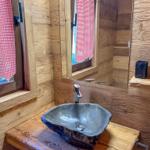 Bad mit Steinwaschbecken, Holzwand und Spiegel mit rotem Gittervorhang.