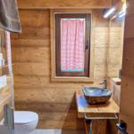 Holzbadezimmer mit Waschbecken, Toilette und Fenster mit rotem Vorhang.