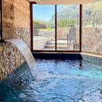 Indoor-Pool mit Wasserfall und Bergblick durch große Fenster.