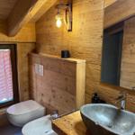 Holzbadezimmer mit Waschbecken, Toilette und Fenster mit kariertem Vorhang.
