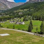 Grünes Tal mit Häusern, Wald und Bergen. Reiter auf Straße. Hubschrauberlandeplatz.