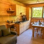 Küche mit Essbereich und Sofa. Holzwände und -möbel. Fenster mit Blick auf Grün.