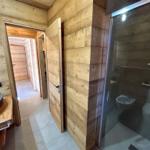 Badezimmer mit Holzwand, Dusche, Waschbecken und Toilette.