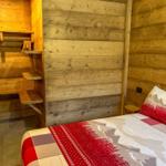 Schlafzimmer mit Holzwand und Bett mit Bergmotivdecke.