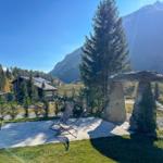 Terrasse mit Liegestuhl und Steinmonolithen vor Berglandschaft.
