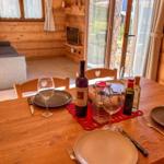 Holztisch mit Geschirr und Flaschen im Essbereich. Hintergrund: Wohnzimmer mit Sofa und TV.