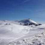 Schneebedeckte Berghänge mit Ski- und Snowboardpisten unter blauem Himmel.