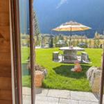 Durch die Glastür blickt man auf eine grüne Terrasse mit Tisch, Sonnenschirm und Hund.