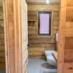 Holzbadezimmer mit Toilette, Waschbecken und Fenster mit rotem Gitter.