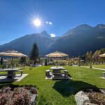 Grüner Garten mit Steinbänken, Sonnenschirmen und Bergblick.