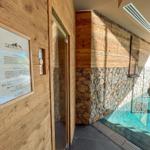 Sauna mit Holzwand und Steinwand, Blick auf Pool und Berglandschaft.
