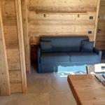 Ein Wohnzimmer mit einem grauen Sofa, Holzwänden und einem Esstisch mit Platz für zwei.