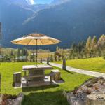 Terrasse mit Tisch, Sonnenschirm und Blick auf grüne Wiesen und Berge.
