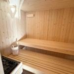 Sauna mit Holzbank und Holzrahmen, ein Holzeimer und ein Holzofen sind sichtbar.