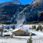 Haus mit Steinmauer und Holzverkleidung im Schnee, umgeben von Bergen und Wald.