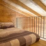 Schlafzimmer mit Holzwand und Dachschrägen, Bett mit Bergmotiv.