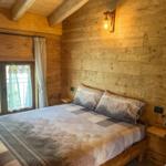 Schlafzimmer mit Holzwänden, Bett mit Bergmotiv und Fenster mit Blick auf Wald.