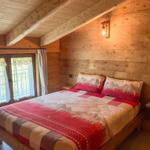 Schlafzimmer mit Holzwand, Bett und Fenster zur Terrasse.