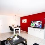 Wohn- und Essbereich mit roter Wand, TV und Esstisch.