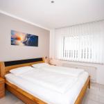 Schlafzimmer mit Doppelbett, Nachttischen und Fenster mit Jalousie.