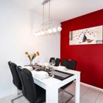 Esszimmer mit weißem Tisch, schwarzen Stühlen und roter Wand. Deckenleuchte und Wandbild.
