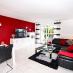 Wohn- und Essbereich mit roter Wand, schwarzen Ledersofas und Glas-Tisch.