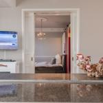 Wohnbereich mit Fernseher und Blick in Schlafzimmer mit Kronleuchter.