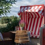Rote Strandkörbe mit Streifen, Tisch und Stühle auf Terrasse mit Blick auf Grün und Wasser.