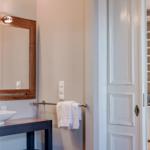 Badezimmer mit Spiegel und Handtuchhalter. Durchgang zur Küche mit Schränken.