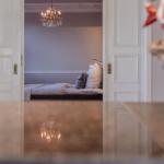 Schlafzimmer mit Bett, Kissen und Kronleuchter. Durchgehendes Licht und hölzernes Bodenbelag.