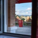 Blick vom Fenster auf eine Terrasse mit rotem Pflanzkübel und Seestrand.
