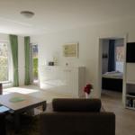 Wohnzimmer mit Sofa, Couchtisch und Blick auf Garten. Fernseher und Schlafzimmer sichtbar.