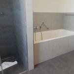 Bad mit Dusche und Badewanne, graue Fliesen und Chromarmaturen.