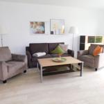 Wohnzimmer mit Sofa, zwei Sesseln, Couchtisch und Wandbildern.