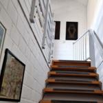 Treppe mit Holzstufen und weißen Wänden, an denen Bilder hängen.