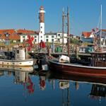 Hafen mit Booten, Leuchtturm und Häusern am Wasser.