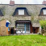 Haus mit Strohdach, Garten und Terrasse mit Gartenmöbeln.