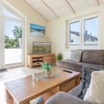 Wohnzimmer mit Sofa, Couchtisch und TV. Große Fenster und Holzdecke.