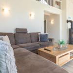 Großer Wohnbereich mit Sofa, Couchtisch und Kaminofen. Küche im Hintergrund.