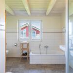 Badezimmer mit Badewanne, Fenster und Dusche. Holzdecke und Fliesen.